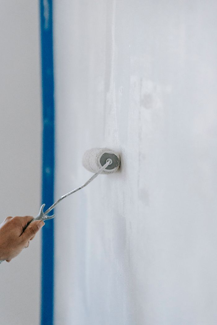 services-04 A close-up of a person using a paint roller to apply white paint on an indoor wall.